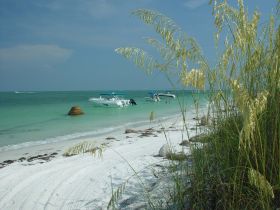 A picturesque beach scene featuring boats anchored near the shore, with people enjoying the water — a perfect spot for relaxation and fun in the sun.