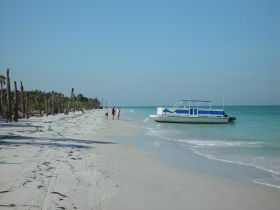 A picturesque beach scene featuring a boat anchored offshore while a group of people enjoys the serene coastline, perfect for a day of relaxation and exploration.