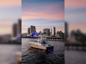 A stunning view of the 'MOONDOG' yacht docked against a vibrant city skyline at sunset, showcasing the perfect blend of urban and nautical beauty.
