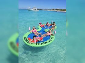 A lively group enjoys a fun day on a floating mat in crystal-clear waters, perfect for summer parties and relaxation under the sun.