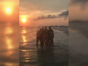 A joyful family poses together in the water at sunset, capturing a memorable beach experience filled with laughter and togetherness.