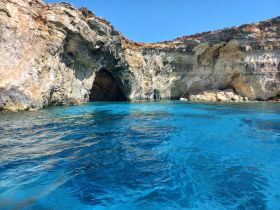 A stunning view of a rocky coastline with a cave entrance, surrounded by crystal-clear blue waters — perfect for exploring natural wonders on a boating adventure.