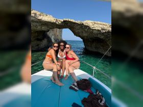 Three friends enjoy a sunny day on a boat, posing together with a stunning rock formation in the background — perfect for memorable beach outings and group celebrations.