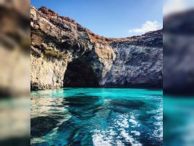 A stunning view of a rocky coastline with a cave entrance, surrounded by crystal-clear turquoise waters — a perfect destination for boat tours and exploration.