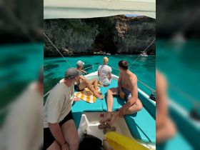 A group of friends relaxes on a boat, enjoying the stunning turquoise waters and a scenic cave view — perfect for adventure seekers and nature lovers.