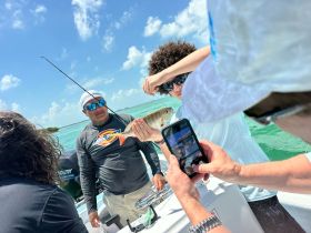 A young angler proudly displays his catch while others capture the moment on their phones — a perfect snapshot of a fun fishing trip on the water.