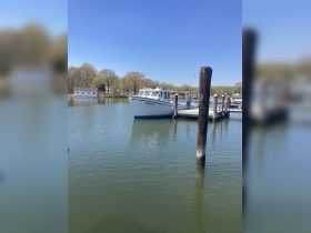 A serene view of the boat named 'Grace' docked peacefully at the marina, surrounded by lush greenery and clear blue skies.
