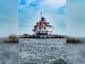 A stunning view of a lighthouse standing on stilts in the water, surrounded by rocky outcrops — a picturesque landmark perfect for boating adventures.