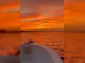 A serene sunset view from the bow of a boat, showcasing vibrant orange skies and calm waters — perfect for evening cruises.