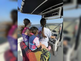 Three children enjoy a fun day on the water, taking turns at the helm of the boat while wearing life jackets — a perfect family boating adventure.