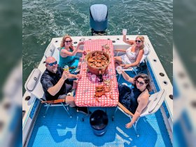 A lively group enjoys a seafood feast on a boat, raising their drinks in celebration — perfect for summer gatherings and memorable outings on the water.