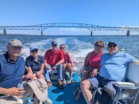 A cheerful group of friends enjoys a boat ride with a stunning bridge in the background, capturing the essence of a perfect day on the water.