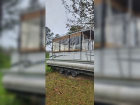 A side view of a pontoon boat with a covered area, showcasing its structure while docked on land, ideal for family outings and leisure activities.