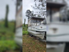 A pontoon boat is docked and ready for use, showcasing its spacious design and covered area, perfect for leisurely outings on the water.