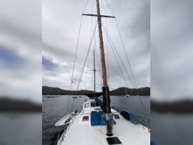A clear view of a sailboat's deck and mast, showcasing its structure against a serene backdrop of water and distant hills.