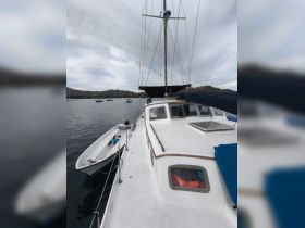 A clear view of a sailboat's deck and hull, showcasing its structure against a serene backdrop of calm waters and distant hills.