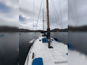 A clear view of a sailboat's deck, showcasing its structure and design against a backdrop of calm waters and distant hills — perfect for sailing enthusiasts.