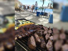 Delicious grilled meats and vegetables are prepared on the beach, perfect for a memorable outdoor dining experience during a boat trip.