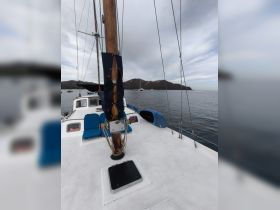 A serene view of a sailboat's deck, showcasing its wooden mast and blue seating against a backdrop of calm waters and distant hills.
