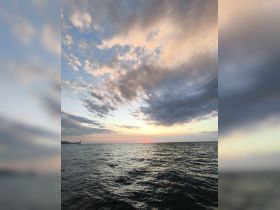 A serene sunset view over the ocean, with a distant sailboat silhouetted against the vibrant sky — perfect for capturing the beauty of evening cruises.