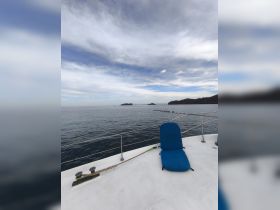 A serene view from the deck of a boat, showcasing a blue lounge chair and calm waters, perfect for relaxation and enjoying the scenic coastline.