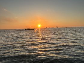 A picturesque sunset view with a fishing boat cruising across the ocean, creating a serene atmosphere perfect for evening adventures on the water.