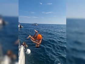 A child performs an impressive flip into the water while another person swims nearby, capturing the joy of summer fun on the water.