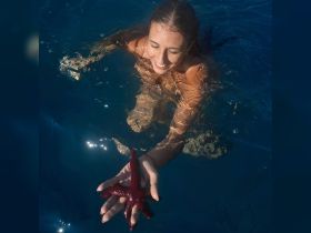 A joyful swimmer interacts with a vibrant red starfish in crystal-clear waters, showcasing the beauty of marine life during a memorable aquatic adventure.