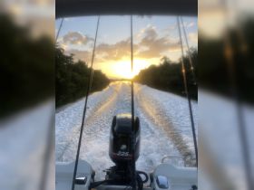 A stunning view from the back of a boat as it speeds through the water at sunset, showcasing the beautiful wake and serene surroundings.