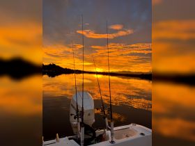 A serene sunset view from a fishing boat, showcasing the tranquil waters and fishing rods, perfect for evening fishing trips.