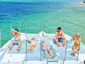 A group enjoys a sunny day on the deck of a boat, relaxing and sunbathing — perfect for a fun day out on the water.