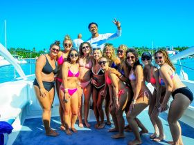 A lively group of friends poses for a fun photo on a boat, celebrating their day on the water in stylish swimwear — perfect for summer adventures and memorable outings.