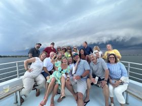 A lively group of friends enjoys a boat party, capturing joyful moments against a dramatic sky — perfect for celebrations and gatherings on the water.