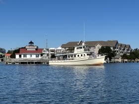The 'Crystal Dawn' yacht is docked near a charming lighthouse and waterfront buildings, showcasing a picturesque boating scene.