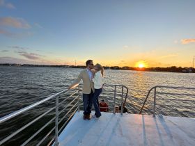 A couple shares a romantic kiss on the deck of a yacht at sunset, creating a perfect backdrop for memorable moments and celebrations on the water.