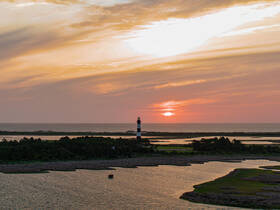 A stunning sunset view featuring a lighthouse along the coastline, creating a picturesque scene perfect for nature lovers and photography enthusiasts.