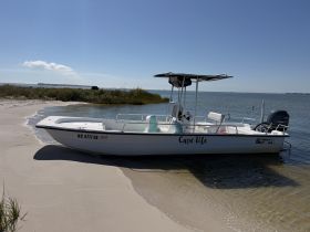 A center console boat named 'Cape Life' is docked on a sandy beach, surrounded by calm waters and lush greenery, perfect for a day of exploration.