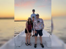 A joyful family poses together on the bow of a boat during a stunning sunset, capturing a memorable moment on the water.