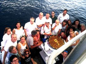 A lively group gathers on a boat to celebrate with a delicious paella, showcasing the joy of dining and camaraderie on the water.