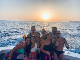 A lively group of friends enjoys a sunset celebration on a boat, complete with drinks and smiles, capturing the essence of a perfect party at sea.