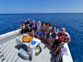 A lively group enjoys a boat party with delicious paella and drinks, creating unforgettable memories on the open water.