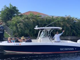 A lively group enjoys their time aboard a Scarab boat, with a friendly captain waving to the camera — perfect for family outings and fun on the water.