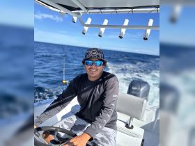 A smiling captain navigates a boat through the open ocean, showcasing the thrill of fishing adventures on the water.