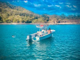 A vibrant scene capturing a boat anchored near a beautiful coastline, with swimmers enjoying the clear waters — perfect for a day of fun and relaxation on the beach.
