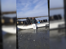 A person stands beside a boat loaded with equipment, showcasing an outdoor fishing adventure in a serene coastal setting.