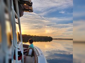 A serene sunset view from a boat featuring a child enjoying the peaceful waters, capturing a perfect moment of tranquility on the water.