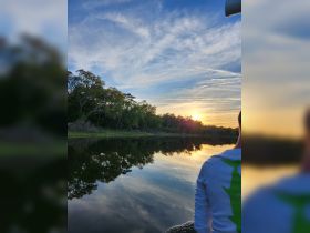 A serene sunset view reflecting on calm waters, with a person enjoying the peaceful scenery — perfect for nature lovers and sunset cruises.