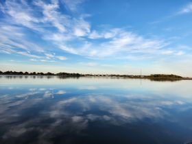 A serene landscape reflecting the sky and trees on calm waters, perfect for capturing the tranquility of nature.