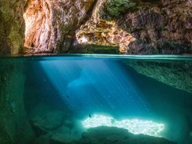 A stunning underwater view of a cave, illuminated by rays of sunlight filtering through the water, creating a magical atmosphere perfect for exploring natural wonders.