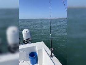 A view of fishing gear and a blue bucket on a boat, showcasing the essentials for a day of fishing on the water.